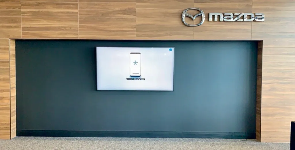 Flat-screen display mounted in a recessed dark feature wall with wood paneling in a car dealership showroom