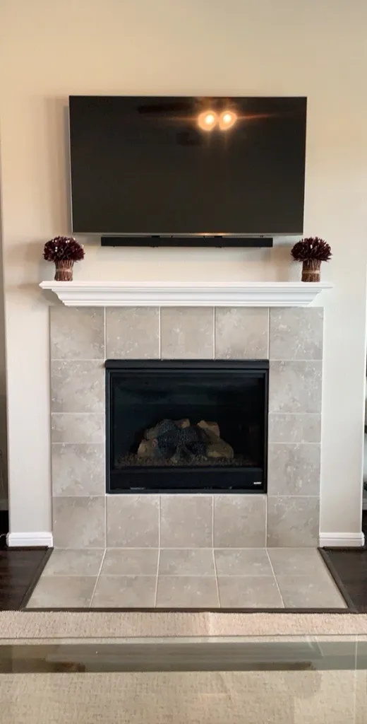 TV and soundbar mounted above a white mantel and tiled gas fireplace with no visible wires
